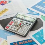 A calculator and real estate flyers depicting financial planning for home buyers.
