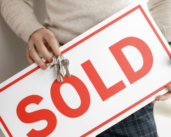 pexels-photo-7642006-7642006 Close-up of a realtor holding a sold sign and keys, symbolizing successful property sale.